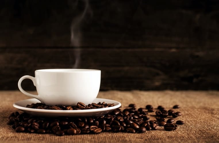 A cup of coffee next to some coffee beans