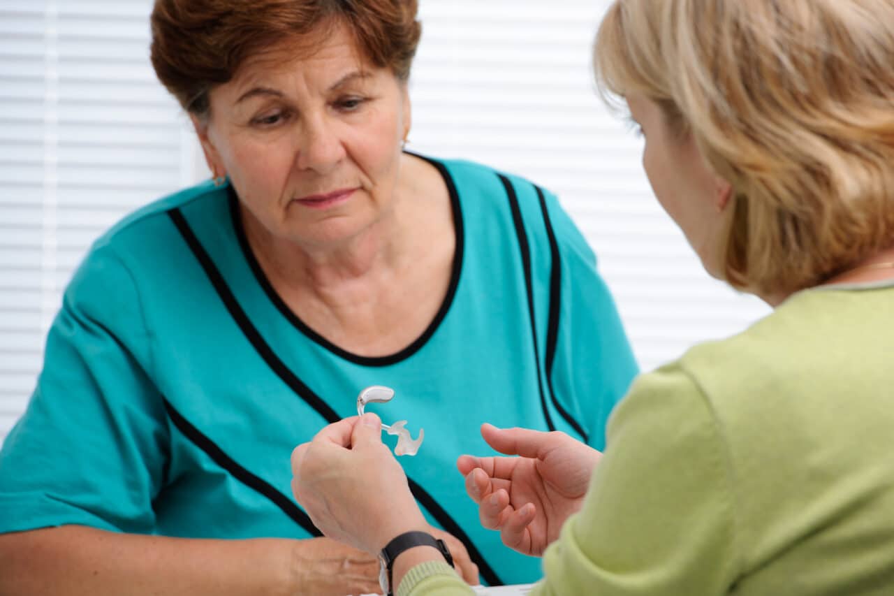 Audiologist showing a hearing aid to a female patient.