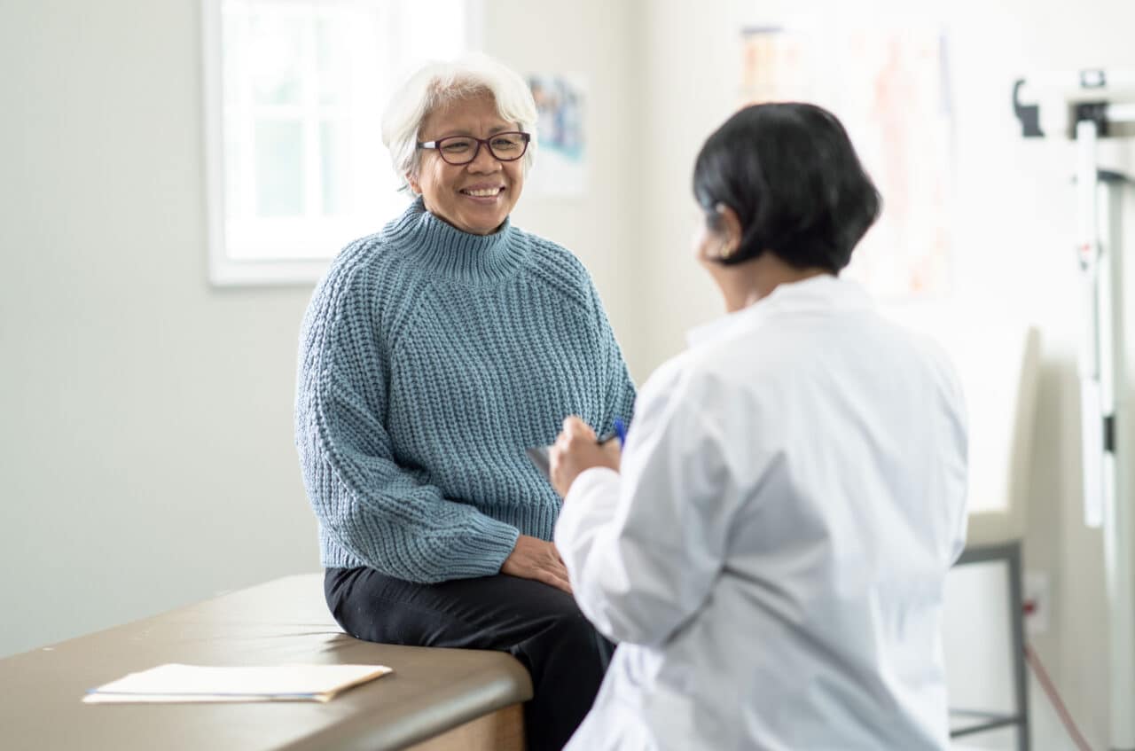 Older female patient sitting on exam table talking with her doctor.