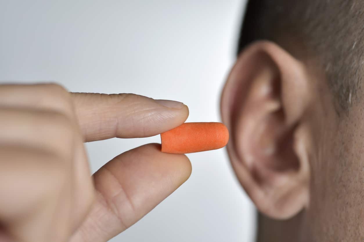 Closeup of a man inserting an orange earplug into his ear.