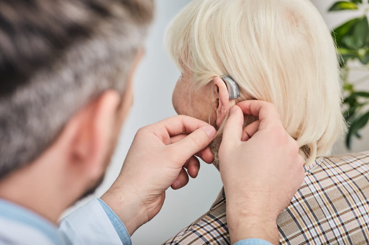 Audiologist fitting an elderly woman with a hearing aid.