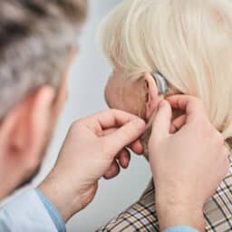 Audiologist fitting an elderly woman with a hearing aid.