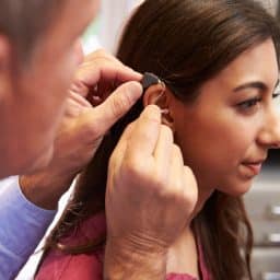 an audiologist fits a woman with hearing aids