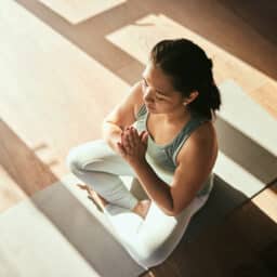 Woman on yoga mat sitting cross-legged meditating