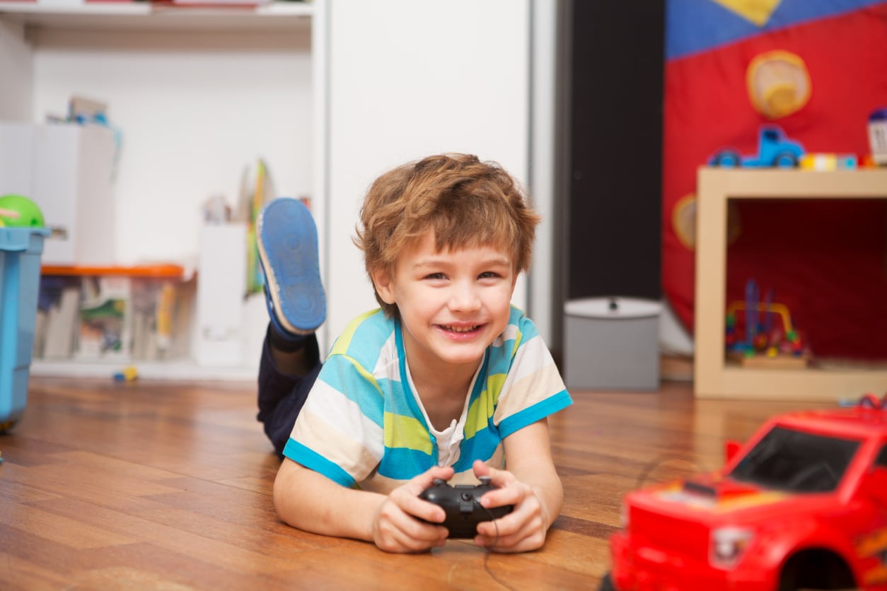 A boy playing with radio-controlled car at home.