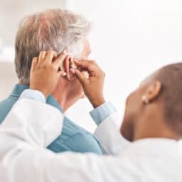 Audiologist fitting a senior man with a hearing aid