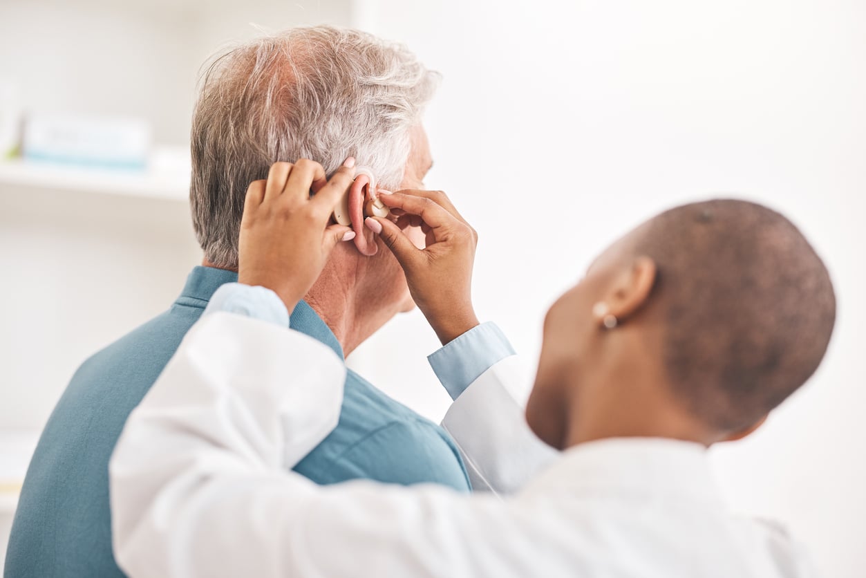 Audiologist fitting a senior man with a hearing aid.