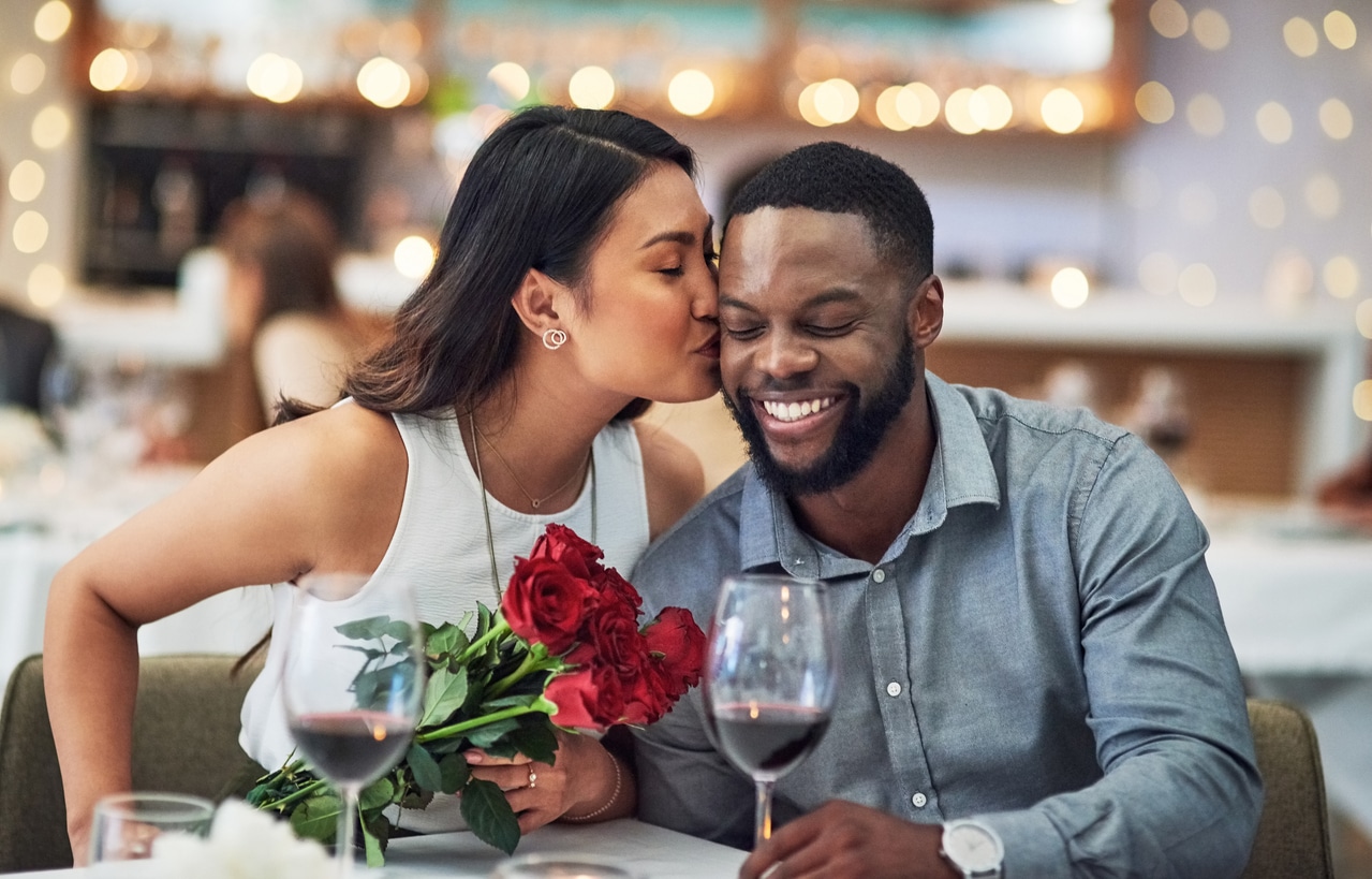 Woman kisses her partner at Valentine's Day dinner with roses.