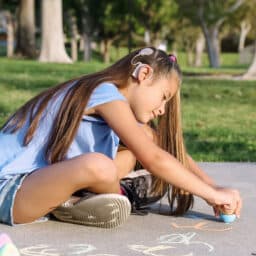 Girl with cochlear implant playing with sidewalk chalk