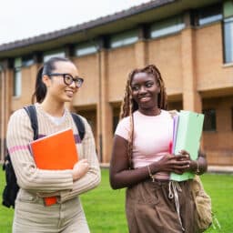 College friends walking across university grounds, carrying textbooks